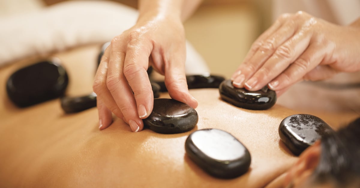 Natural Chronic Pain Relief Strategies - Therapist placing hot stones on customer's back.